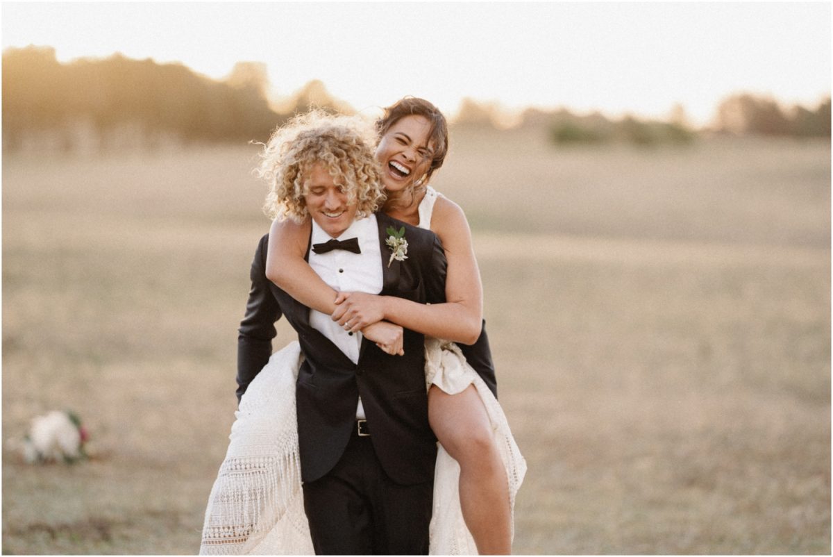 A newly married couple piggy back each other at sunset during their Bendooley Estate Book Barn wedding